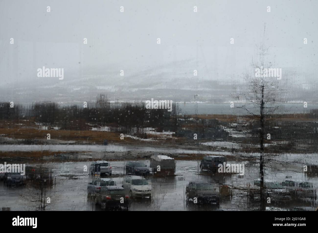 Verre dans un bâtiment couvert de gouttes de pluie, vue sur un parking pluvieux par la fenêtre. Banque D'Images