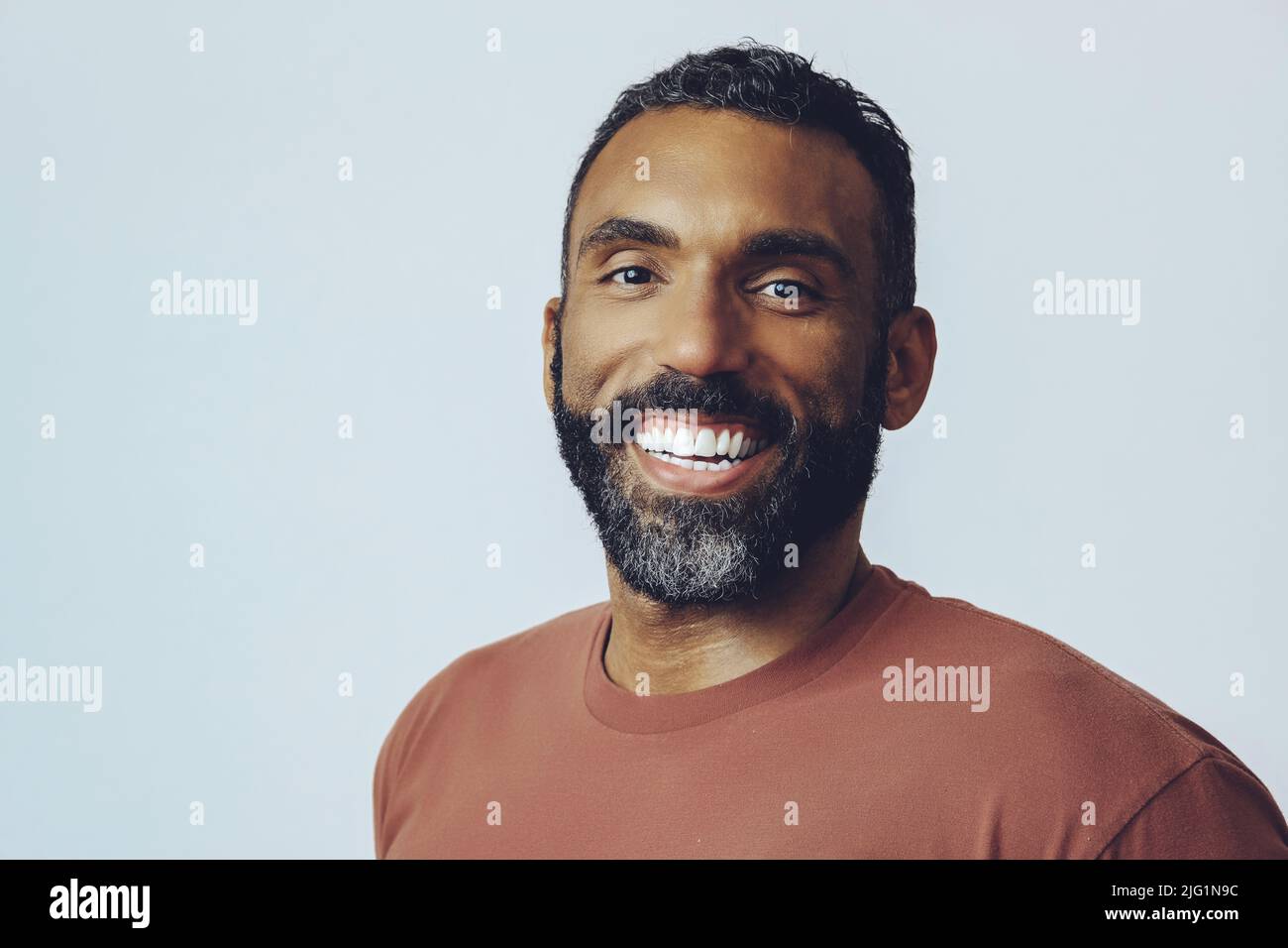 portrait tête d'un beau sourire barbu homme moyen adulte regardant l'appareil photo contre fond gris prise en studio Banque D'Images