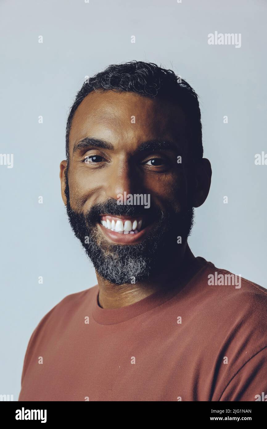 portrait tête d'un beau sourire barbu homme moyen adulte regardant l'appareil photo contre fond gris prise en studio Banque D'Images