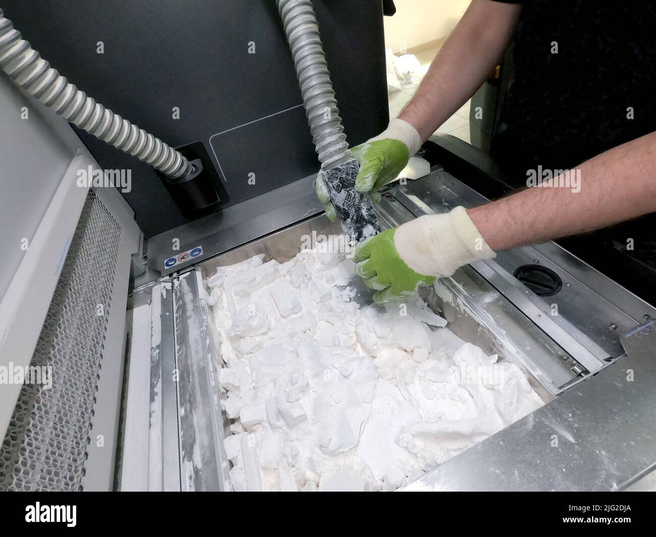 Un homme travaillant avec un aspirateur pour nettoyer la poudre blanche de polyamide à partir d'un modèle imprimé sur une imprimante 3D à l'intérieur d'une imprimante 3D. Objets de nettoyage imprimés sur une imprimante industrielle en poudre 3D Banque D'Images