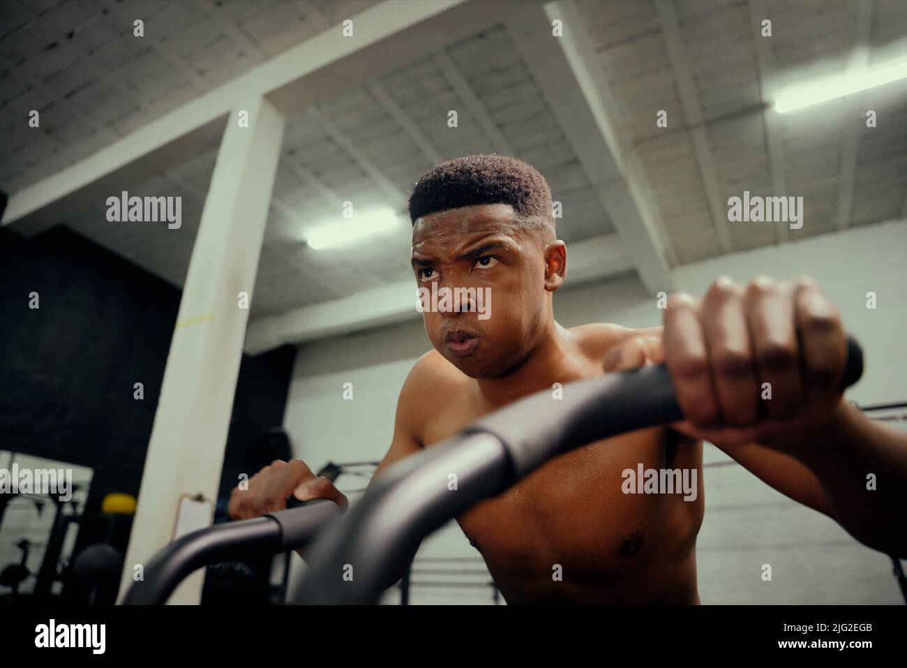 Afro-américain utilisant un entraîneur elliptique pendant l'entraînement de cross-fit. Athlète masculin s'exerçant intensément dans la salle de sport. Photo de haute qualité Banque D'Images