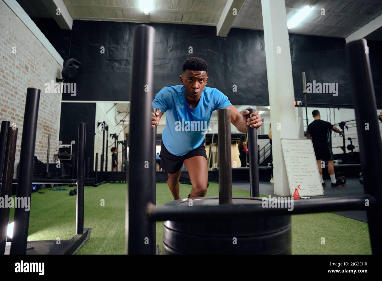 Afro-américain qui s'entraîne intensément lors d'une formation croisée. Athlète masculin poussant le traîneau dans la salle de gym. Photo de haute qualité Banque D'Images