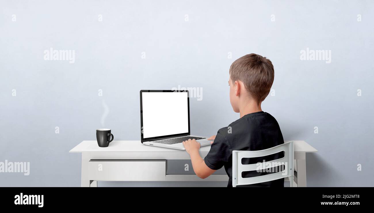 Jeune garçon travaillant sur l'ordinateur portable. Ordinateur portable avec affichage isolé pour la promotion de pages Web. Vue arrière avec espace de copie sur le mur Banque D'Images