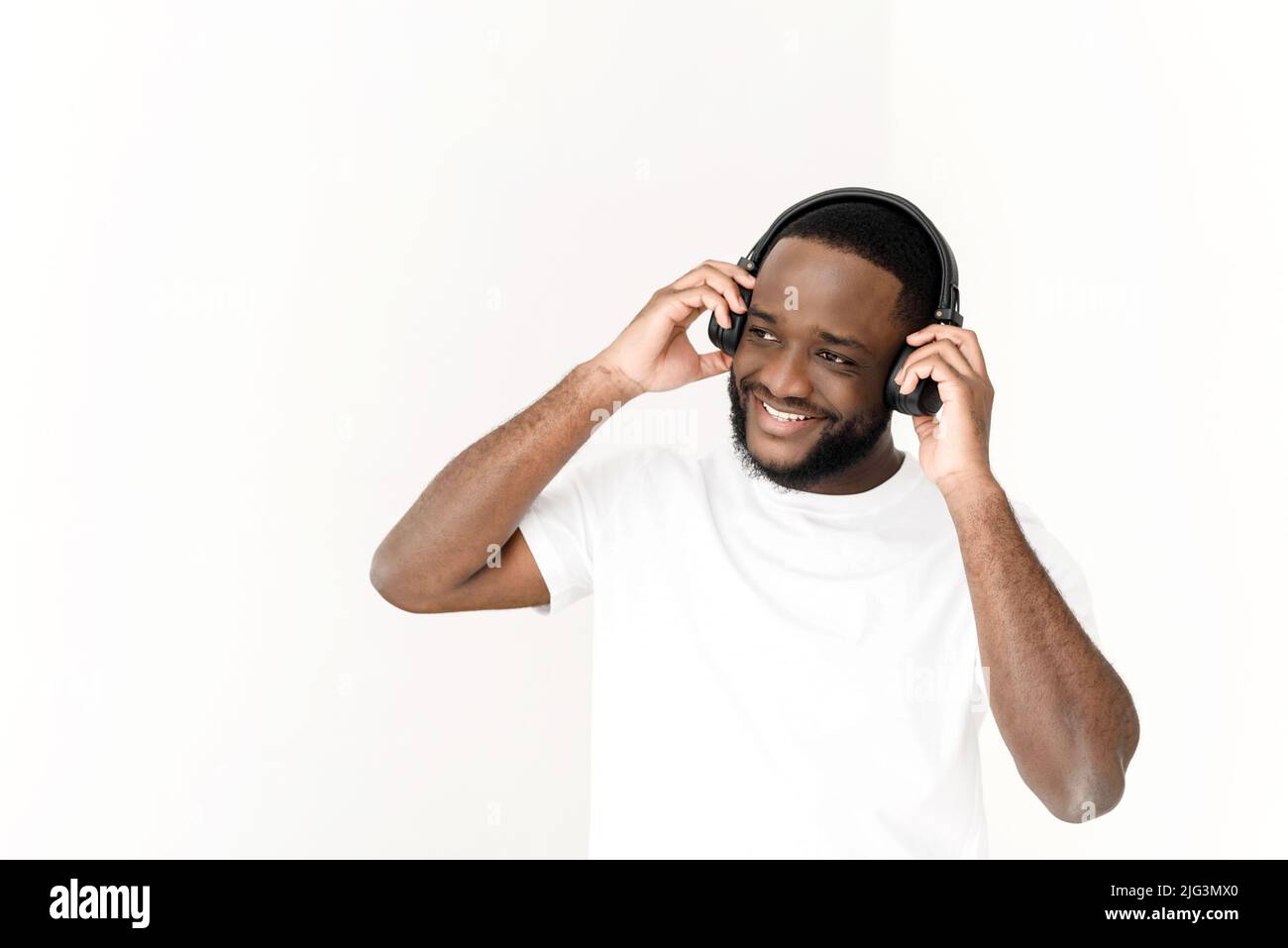 Jeune homme noir appréciant de la musique dans un casque sans fil et chantant sur fond blanc. Banque D'Images