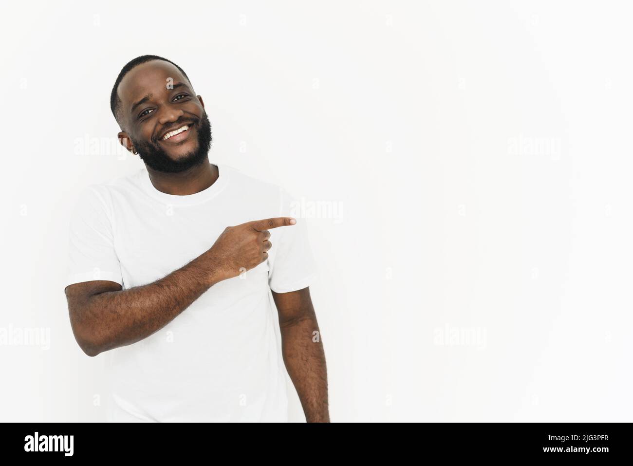 Souriant africain américain homme en t-shirt blanc pointant avec le doigt sur le côté à l'espace de copie pour votre annonce de texte faisant la promotion de votre produit en arrière-grou blanc Banque D'Images