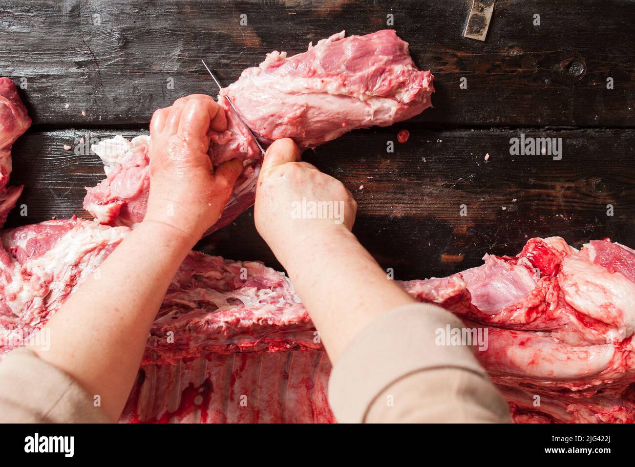 Le boucher coupe la viande de porc crue. Fond en bois Banque D'Images