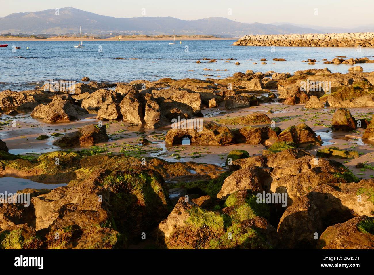 Vue sur le paysage à travers la baie de Santander Cantabria Espagne avec des yachts amarrés et un groin de roche en début de matinée soleil d'été Banque D'Images