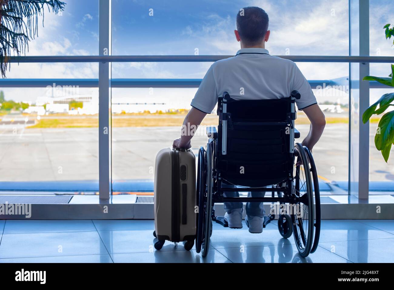 Jeune homme en fauteuil roulant avec bagages à l'aéroport de proximité Banque D'Images