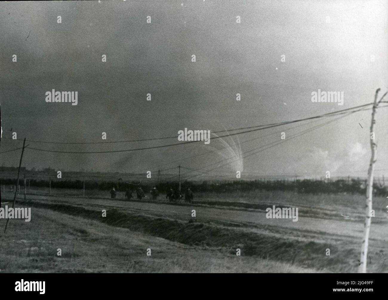 L'équipe des soldats. Sept soldats, marchant dans la ligne à travers la gouttière d'une route. En arrière-plan, explosions de projectiles. Dans le paysage, les câbles permanents et les circonstances sont appréciés. Banque D'Images