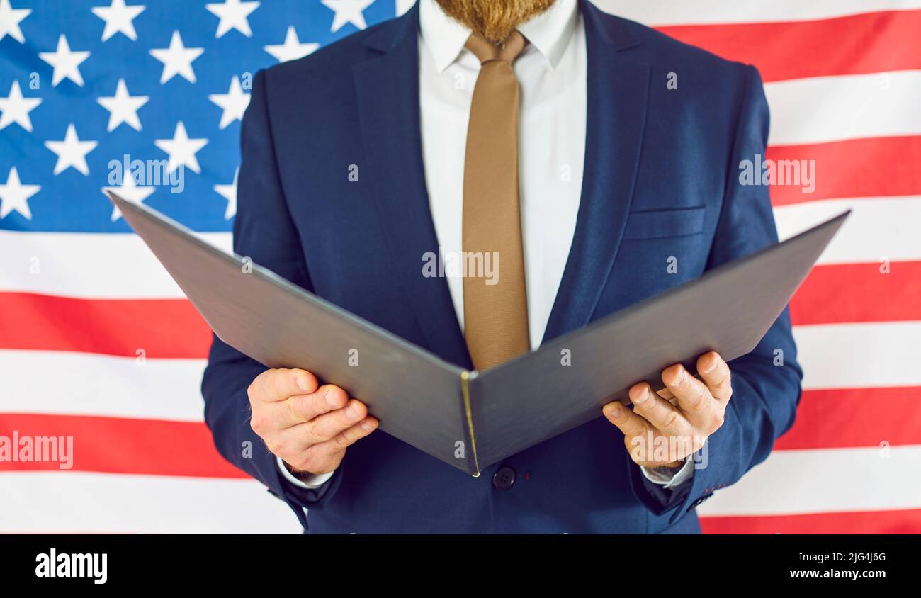 Gros plan du dossier ouvert entre les mains d'un homme inconnu en costume d'affaires sur fond de drapeau américain. Banque D'Images