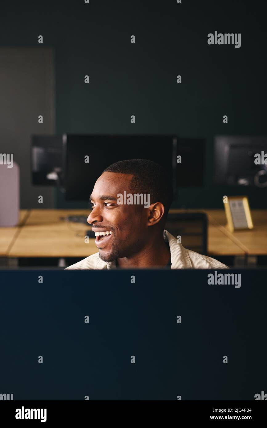 Jeune homme noir travaillant sur un ordinateur dans un bureau moderne, souriant Banque D'Images