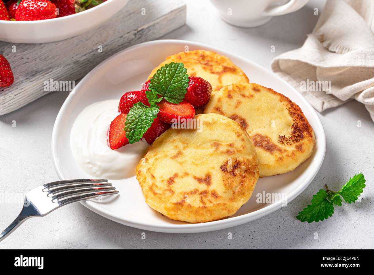 Crêpes au fromage cottage avec fraises et crème dans une assiette blanche sur fond gris clair gros plan. Banque D'Images