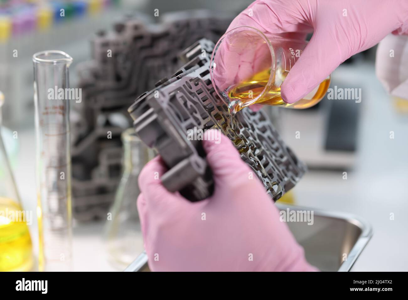 Un scientifique du flacon de produit chimique verse de l'huile sur le corps de soupape de la boîte de vitesses Banque D'Images