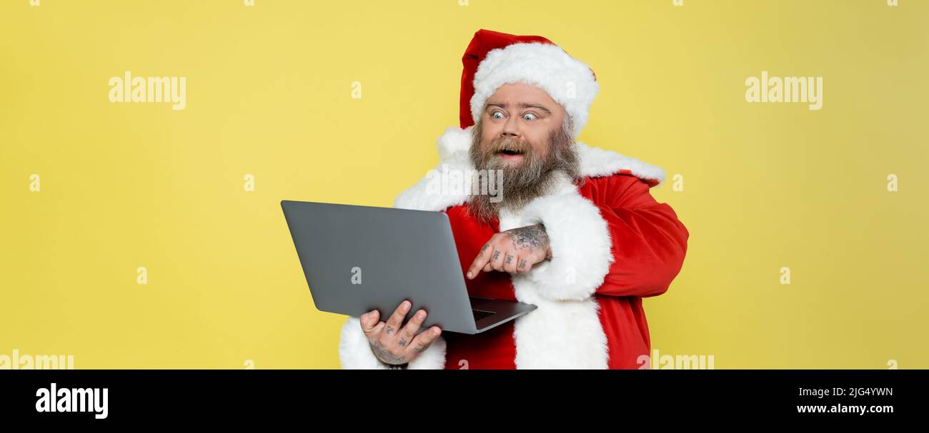un homme excités de plus grande taille en costume de noël pointant vers l'ordinateur isolé sur la bannière jaune Banque D'Images