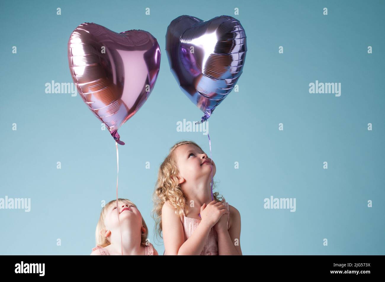 Le bonheur flotte autour de nous. Photo de deux sœurs mignonnes jouant avec des ballons de coeur sur un fond de studio. Banque D'Images