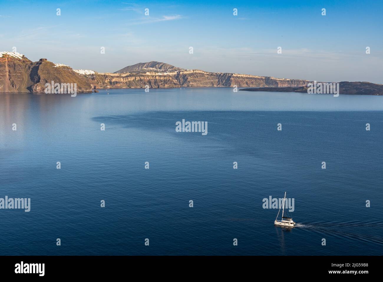 Vue panoramique de Santorin au coucher du soleil avec un catamaran naviguant le long de la côte, Grèce Banque D'Images