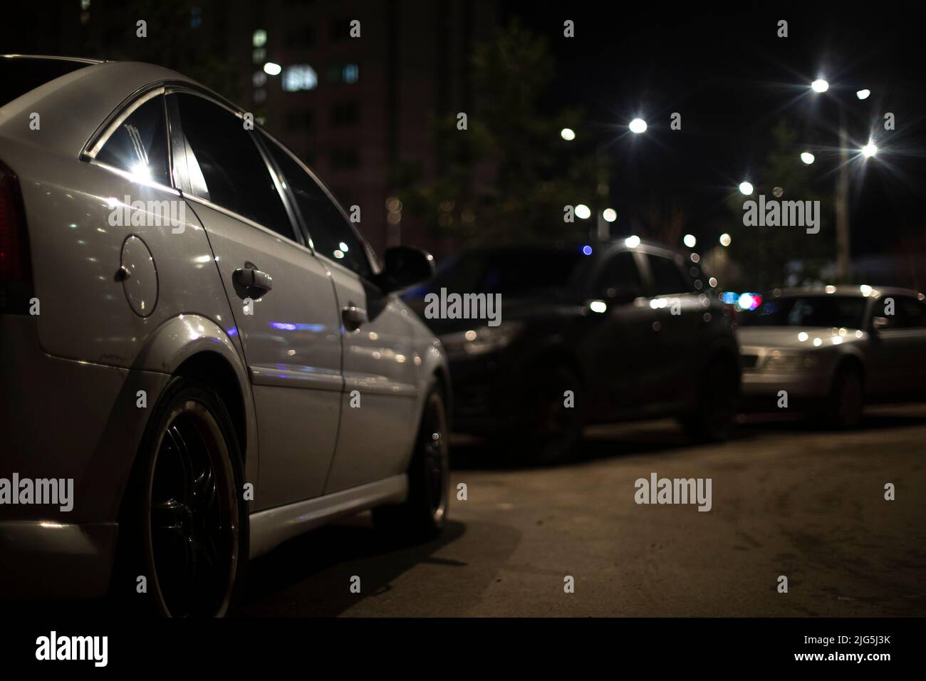 Voiture blanche dans le parking la nuit. Beaucoup de voitures dans la cour. Espace de stationnement et éclairage. Vue latérale de la voiture. Banque D'Images