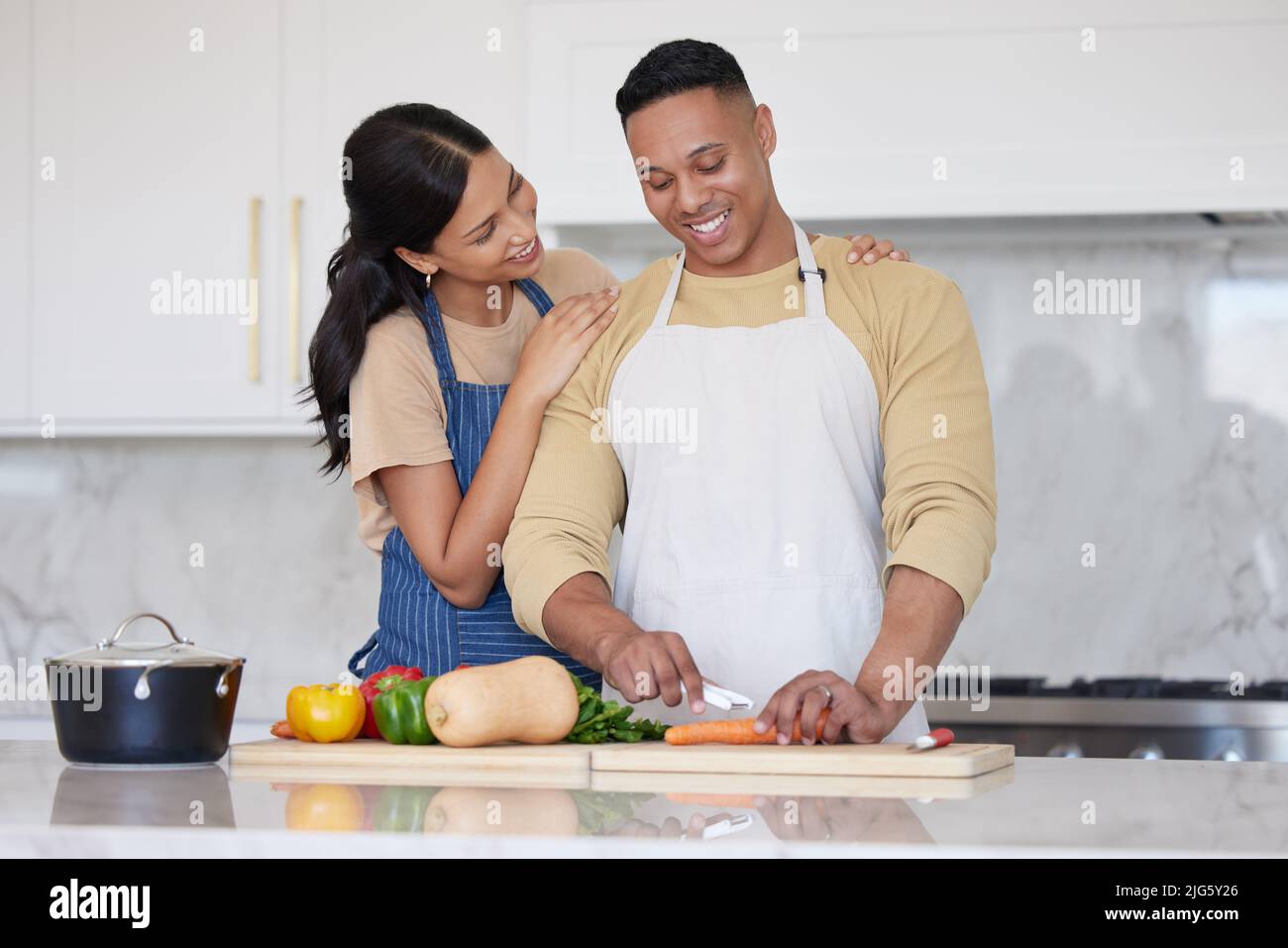 Un jeune couple latin aimant cuisant un dîner sain ensemble à la maison. Un homme aimant coupant des carottes et d'autres aliments de légumes, préparant un repas et Banque D'Images