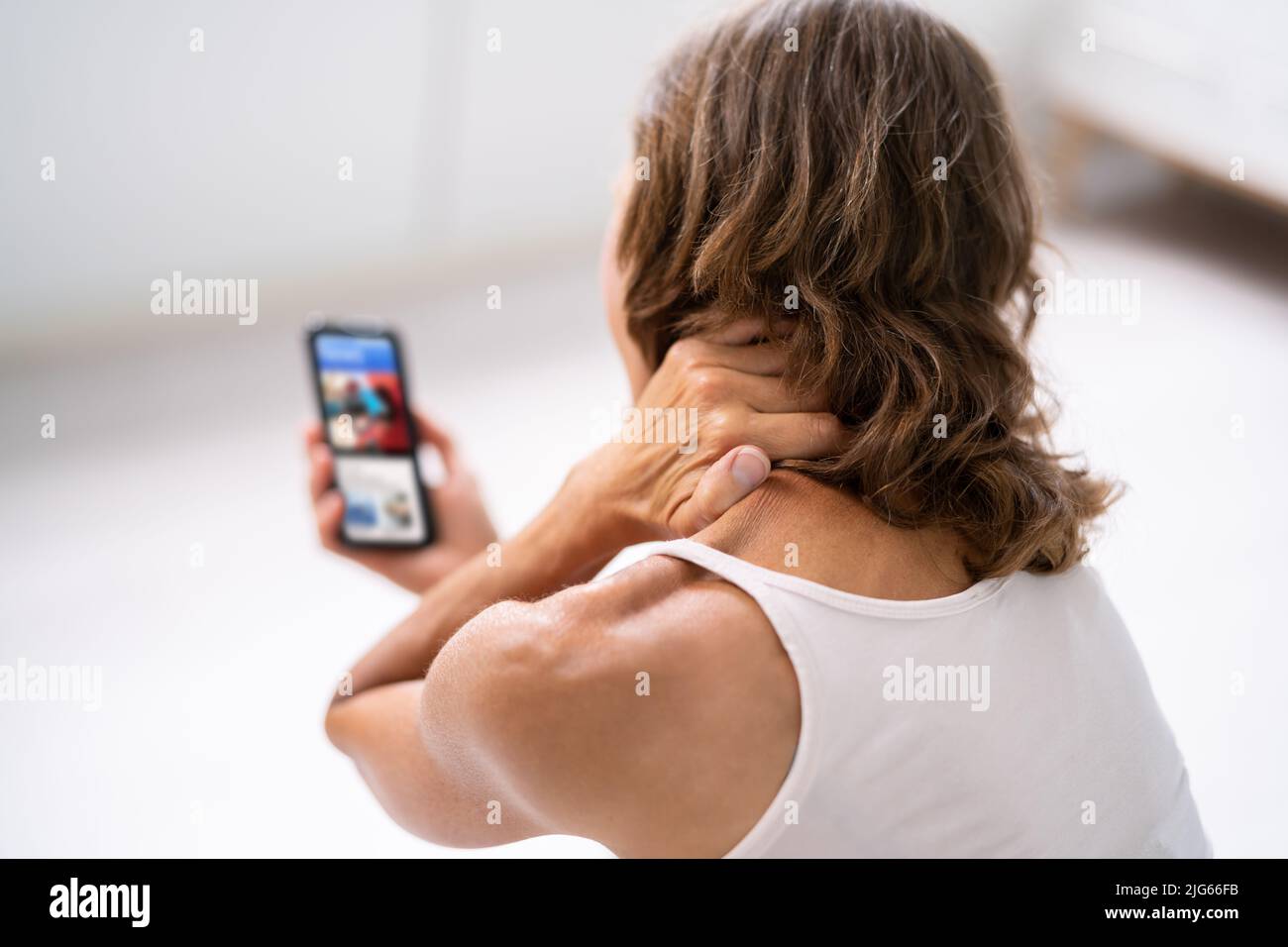 Femme souffrant de douleurs au cou assis à l'aide d'un téléphone portable Banque D'Images