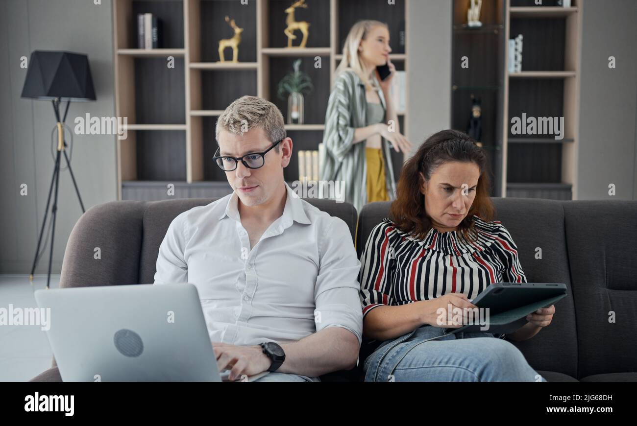 Gadgets addiction. Jeune caucasien de trois tenant et utilisant différents appareils électroniques tout en étant assis sur un canapé dans le salon à la maison . Parents et Banque D'Images