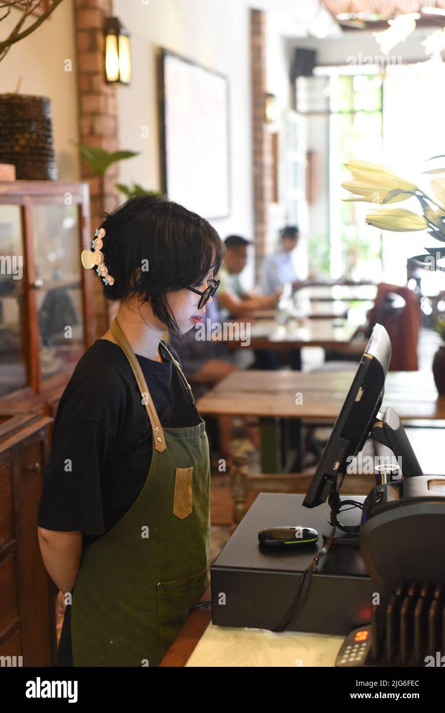 Jeune serveuse vietnamienne servant un client à la caisse dans le café. Banque D'Images