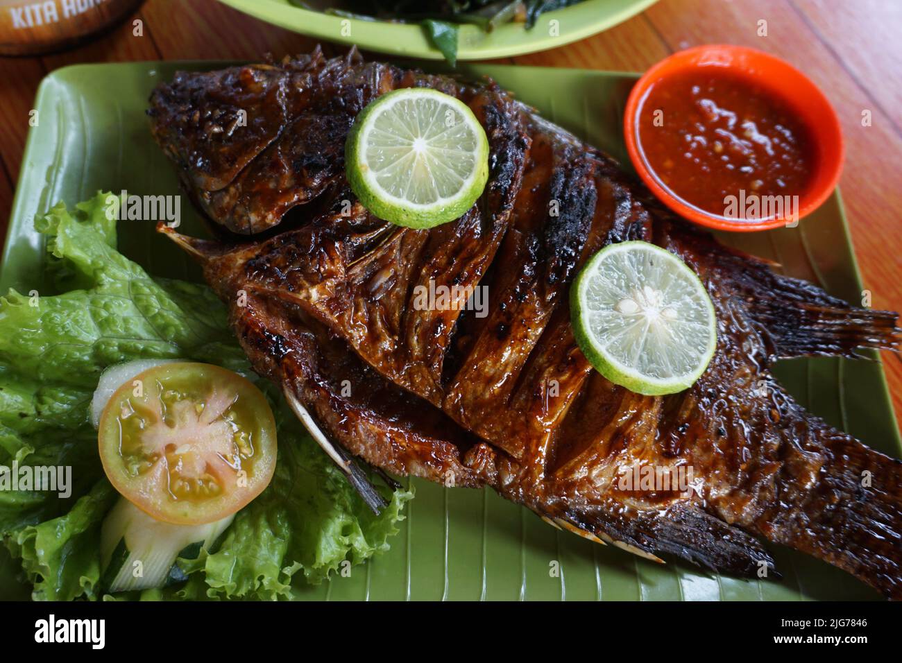 Gourami grillé ou Bakar Gurame avec miel, sauce Chili rouge, légumes et citron sur l'assiette verte. Servi sur la table et prêt pour le déjeuner. Banque D'Images