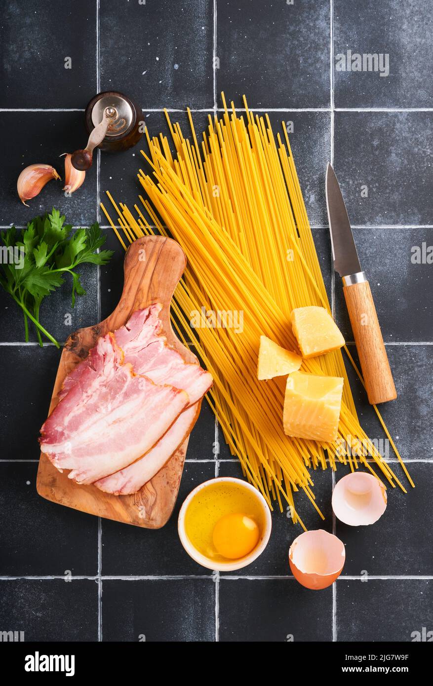 Ingrédients pour pâtes Carbonara. Pâtes italiennes Traidtional Carbonara Ingrédients bacon, spaghetti, parmesan et jaune d'œuf, ail. Table noire en vieux carreaux Banque D'Images