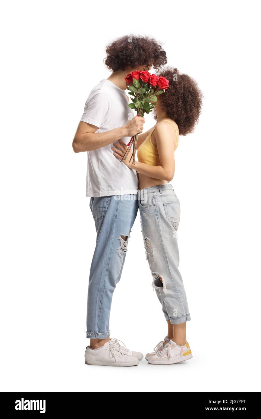 Photo de profil pleine longueur d'un jeune couple décontracté qui embrasse et tient un bouquet de roses rouges isolées sur fond blanc Banque D'Images