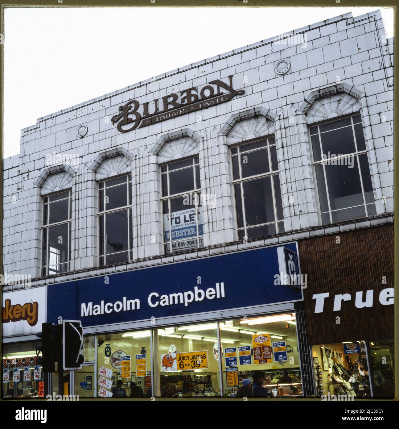 81-95 High Street, Dumbarton, West Dunbartonshire, Écosse, 1970s-1990s. Vue sur l'élévation en pierre blanche de l'ancien magasin Burton au 81-95 High Street, avec des boutiques incluant des greengrocking occupant des unités au rez-de-chaussée. Le magasin Burton, situé au 81-95 High Street, a été construit vers 1937, après la démolition d'un ancien bâtiment (l'hôtel Elephant) en 1935. Des pierres de fondation ont été posées sur le site en 1937 par Arnold James Burton et Stanley Howard Burton. Banque D'Images