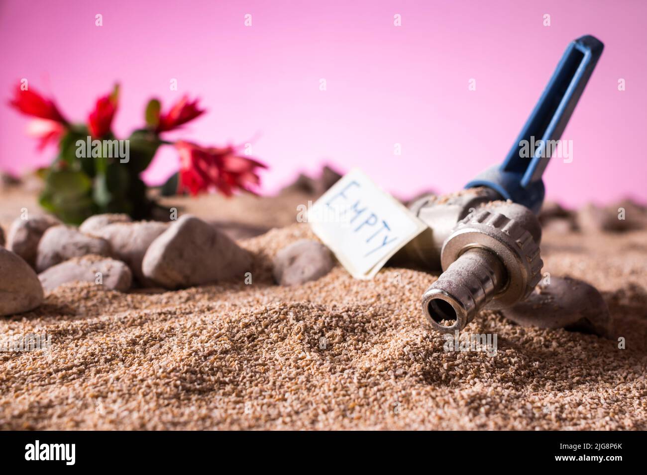Gros plan d'un robinet ouvert et sec enterré par du sable désertique avec une plante succulente contre un fond de ciel rose et sec menaçant avec un panneau vide Banque D'Images