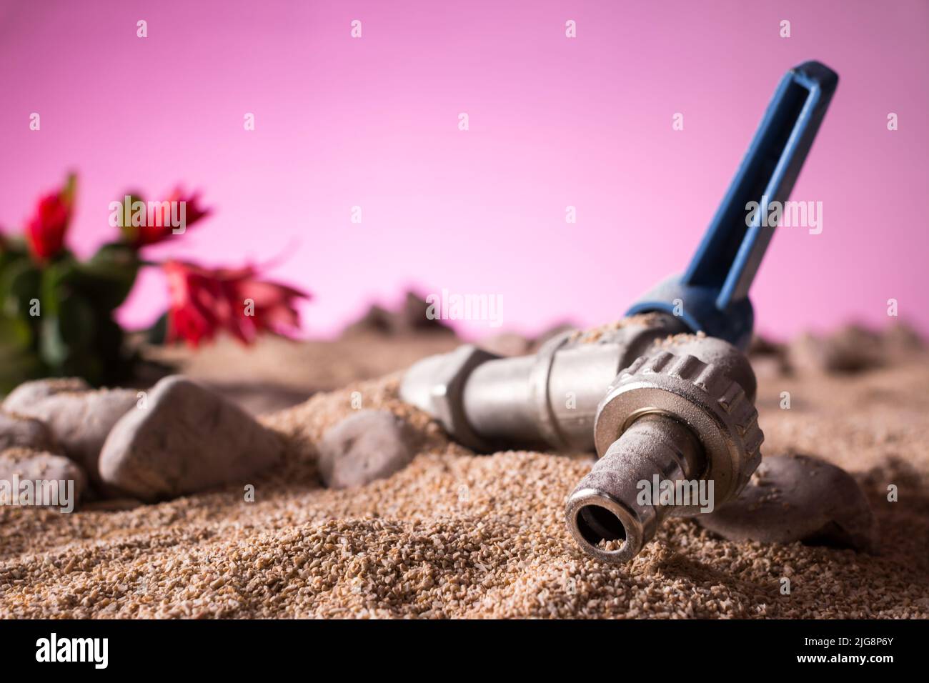 Gros plan d'un robinet ouvert sec enterré par du sable désertique avec une plante succulente sur un fond de ciel rose sec et menaçant Banque D'Images