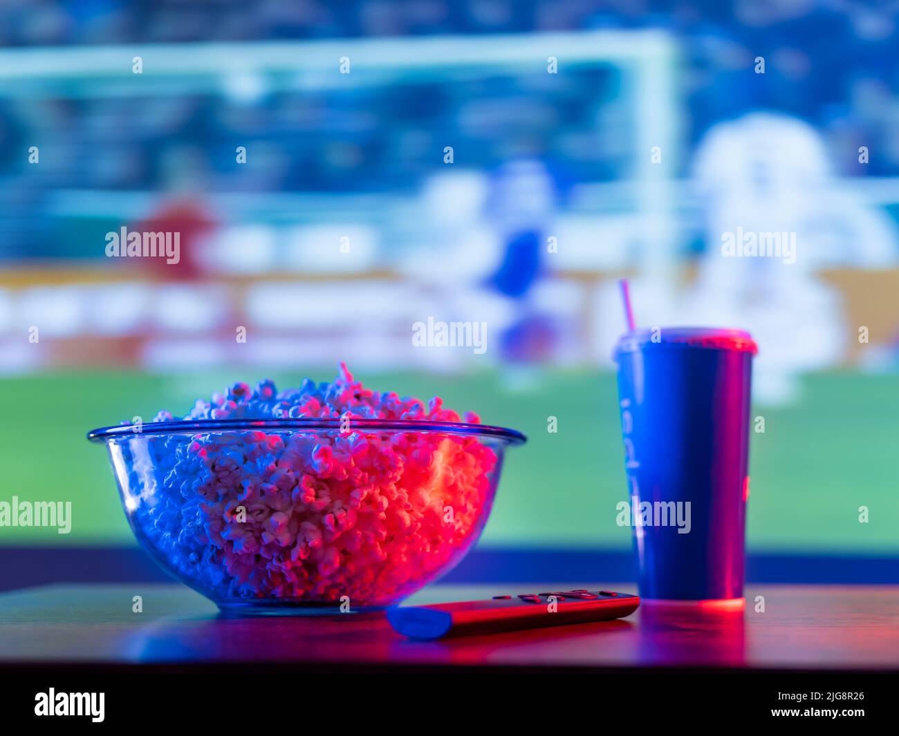Match de football sur grand écran plasma. Sur la table se trouve un bol de pop-corn, une boisson gazeuse dans une tasse en plastique et une télécommande. Regarder des sports pr Banque D'Images