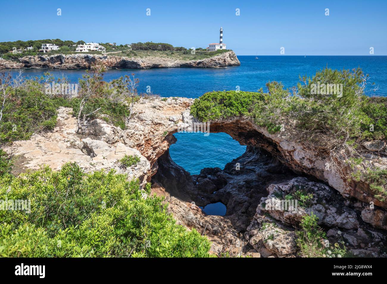 Espagne, Iles Baléares, Majorque, quartier de Felanitx, Portocolom. Sa Cova Foradada, arc naturel de roche et en arrière-plan le phare de Punta de ses Crestes Banque D'Images