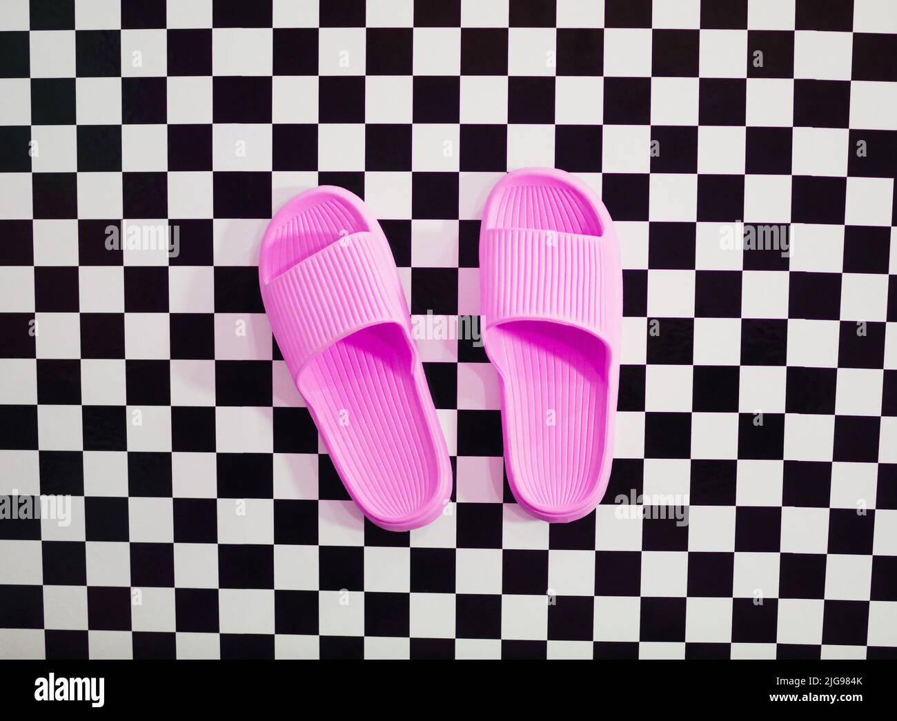 Chaussons roses pour femmes sur fond carré noir et blanc à carreaux. Concept minimal de relaxation. Banque D'Images