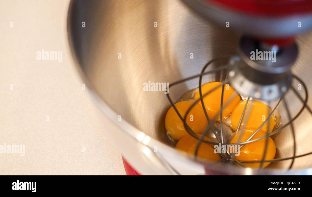 Gros plan sur les œufs jaunes dans un bol mélangeur en métal. Batteur sur socle rouge avec fond blanc. Banque D'Images