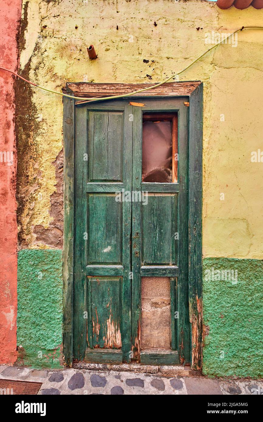 Ancienne porte en bois endommagée d'un bâtiment abandonné aux intempéries. Ancienne entrée verte brisée et vieillie d'une maison dans un petit village ou une ville sur un soleil Banque D'Images