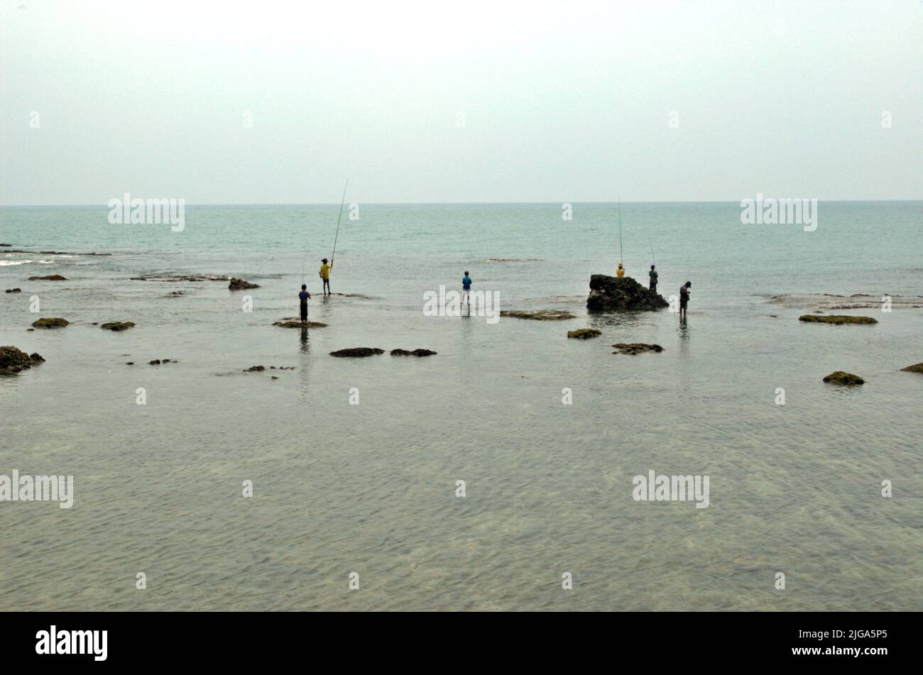 Les gens pêchent en étant debout sur des eaux peu profondes sur une plage plate et rocheuse face au détroit de Sunda à Cikoneng, Anyer, Serang, Banten, Indonésie. Banque D'Images