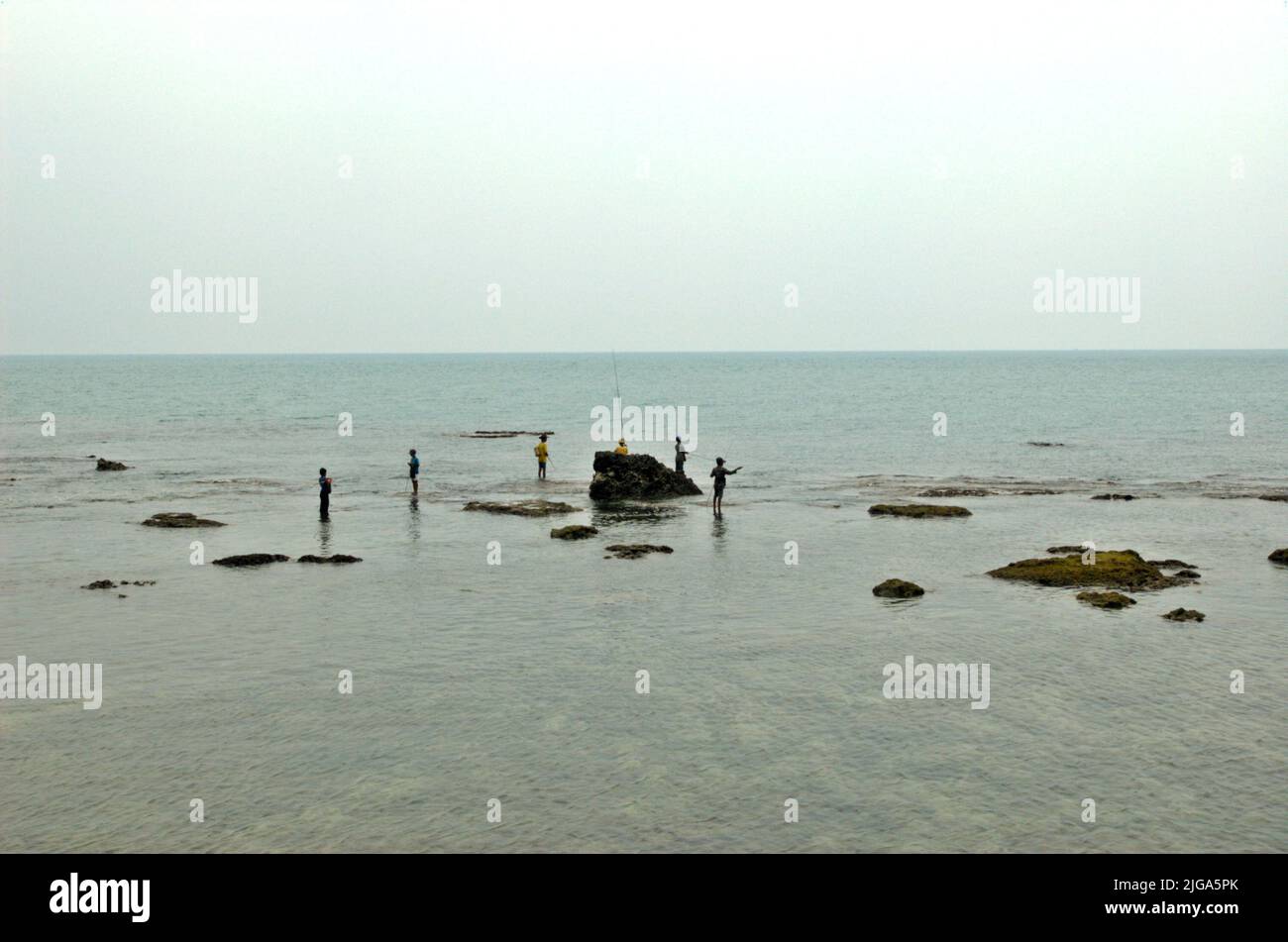 Les gens pêchent en étant debout sur des eaux peu profondes sur une plage plate et rocheuse face au détroit de Sunda à Cikoneng, Anyer, Serang, Banten, Indonésie. Banque D'Images