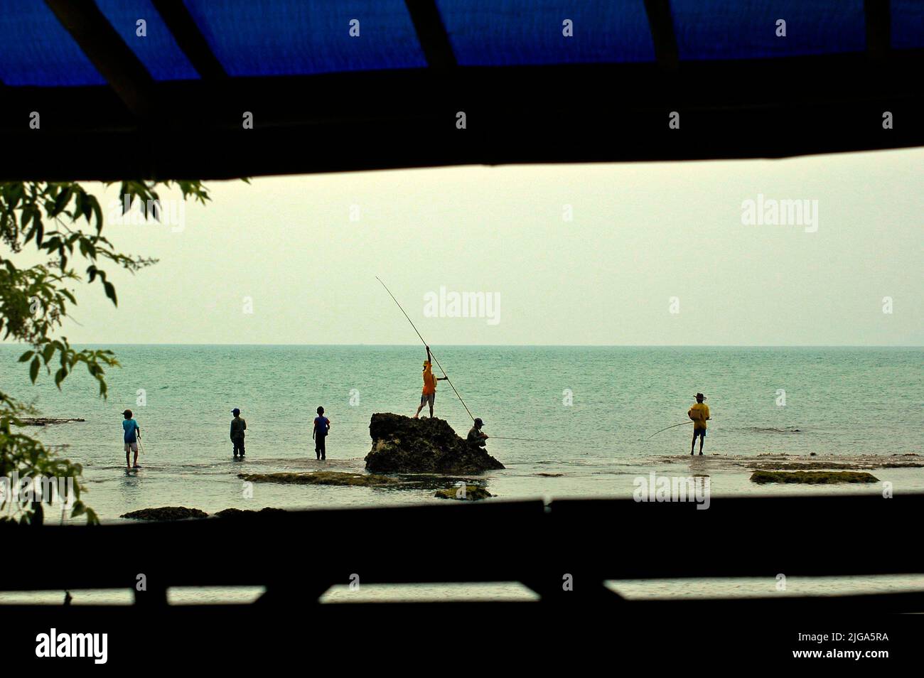 Les gens pêchent en étant debout sur des eaux peu profondes sur une plage rocheuse face au détroit de Sunda à Cikoneng, Anyer, Serang, Banten, Indonésie. Banque D'Images