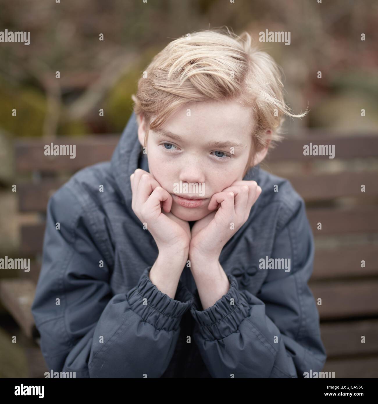 Un jeune adolescent qui a l'air triste et attentionné tout en étant assis seul sur un banc de parc. L'enfant seul se sent mal parce qu'il n'a pas d'amis. Enfant contrarié Banque D'Images