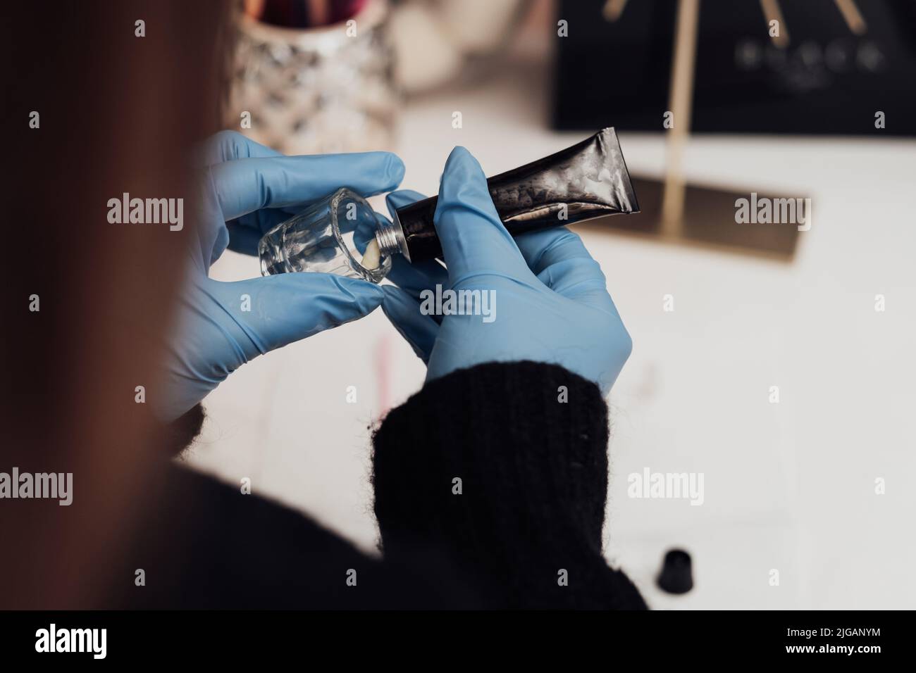 Gros plan de l'artiste de maquillage en gants tire un tube de pâte dans un vaisseau Banque D'Images