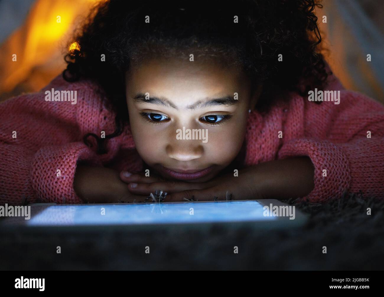 Une adorable petite fille qui utilise une tablette numérique pendant le coucher à la maison. Banque D'Images