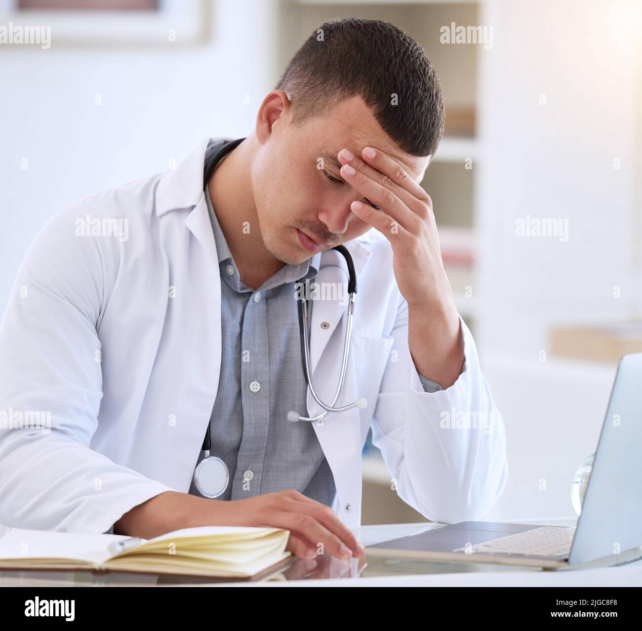 Je n'aurais pas pu avoir de pire nouvelles. Un jeune médecin charmant assis seul dans sa clinique et se sentant stressé en utilisant son ordinateur portable. Banque D'Images