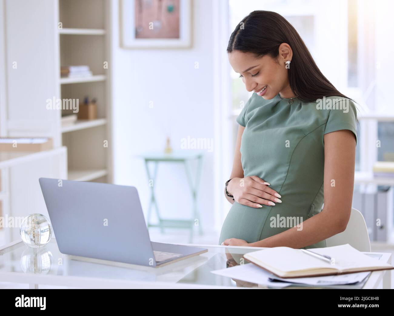 Je peux sentir que vous vous déplacez ici. Une jeune femme d'affaires enceinte assise seule dans le bureau et se frottant le ventre. Banque D'Images