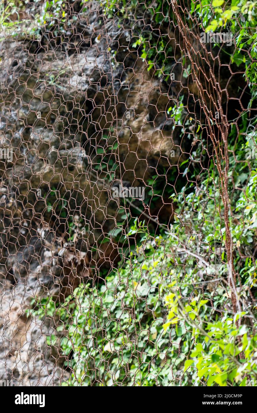 Un maillage de protection en métal couvre les rochers de la chute de roche. Le filet métallique protège la route des glissements de terrain et des chutes de pierres. Équipement de montagne sûr Banque D'Images