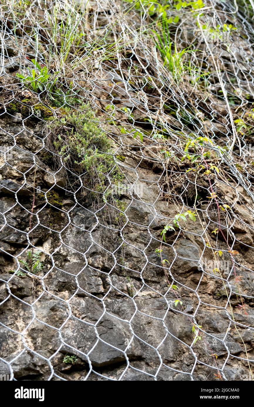 Roche naturelle avec mesh pour se protéger contre les glissements de terrain qui glissent dangereusement le long de la falaise sur la route. Protection contre les chutes de pierres et les chutes de pierres Banque D'Images