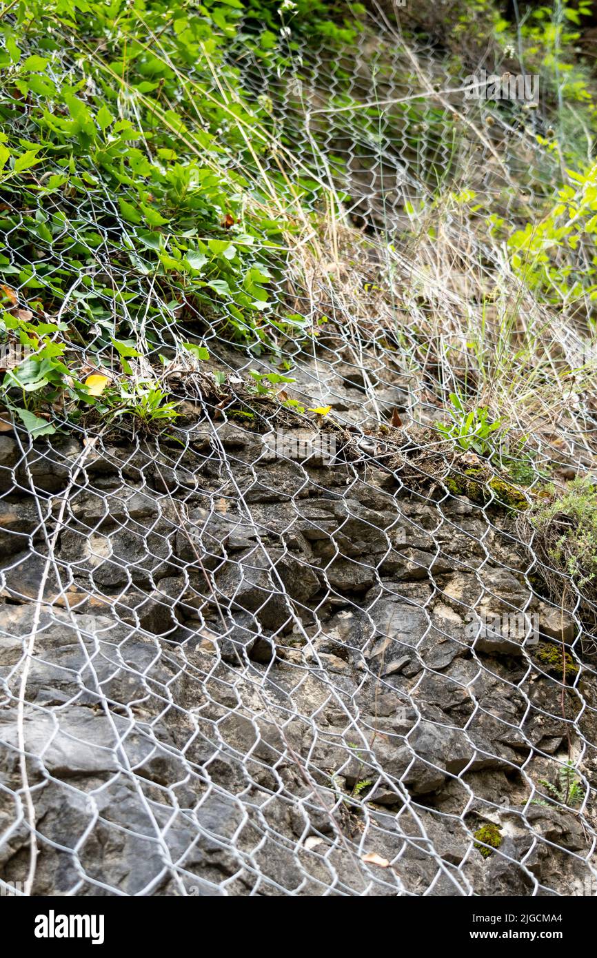 Un maillage de protection en métal couvre les rochers de la chute de roche. Le filet métallique protège la route des glissements de terrain et des chutes de pierres. Équipement de montagne sûr Banque D'Images