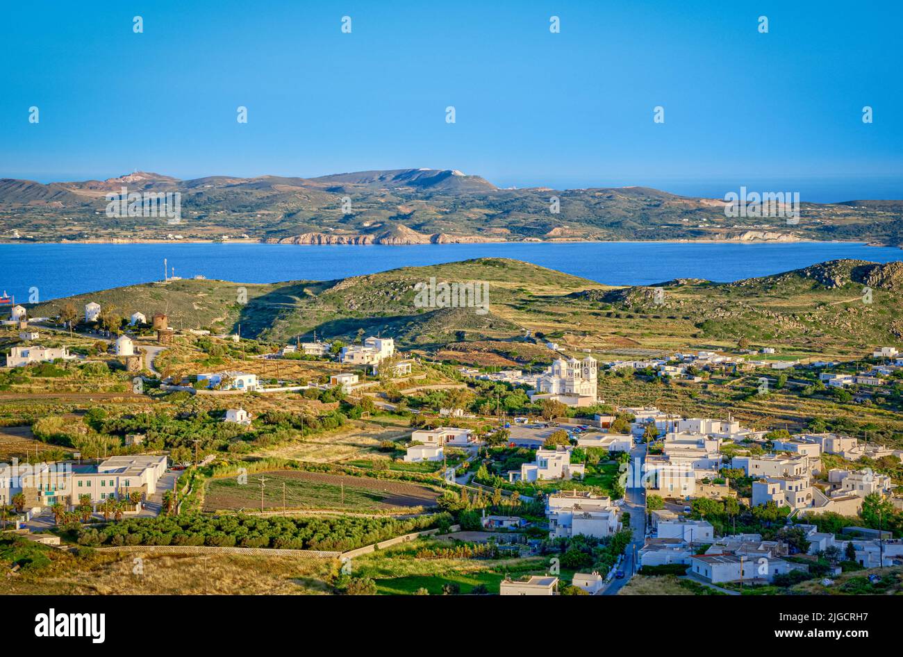 Belle vue sur la ville de Trypiti, la baie et les villages de l'île de Milos au coucher du soleil, Grèce. Maisons blanchies à la chaux, collines vertes, soleil bas, mer bleue, ciel clair, Banque D'Images