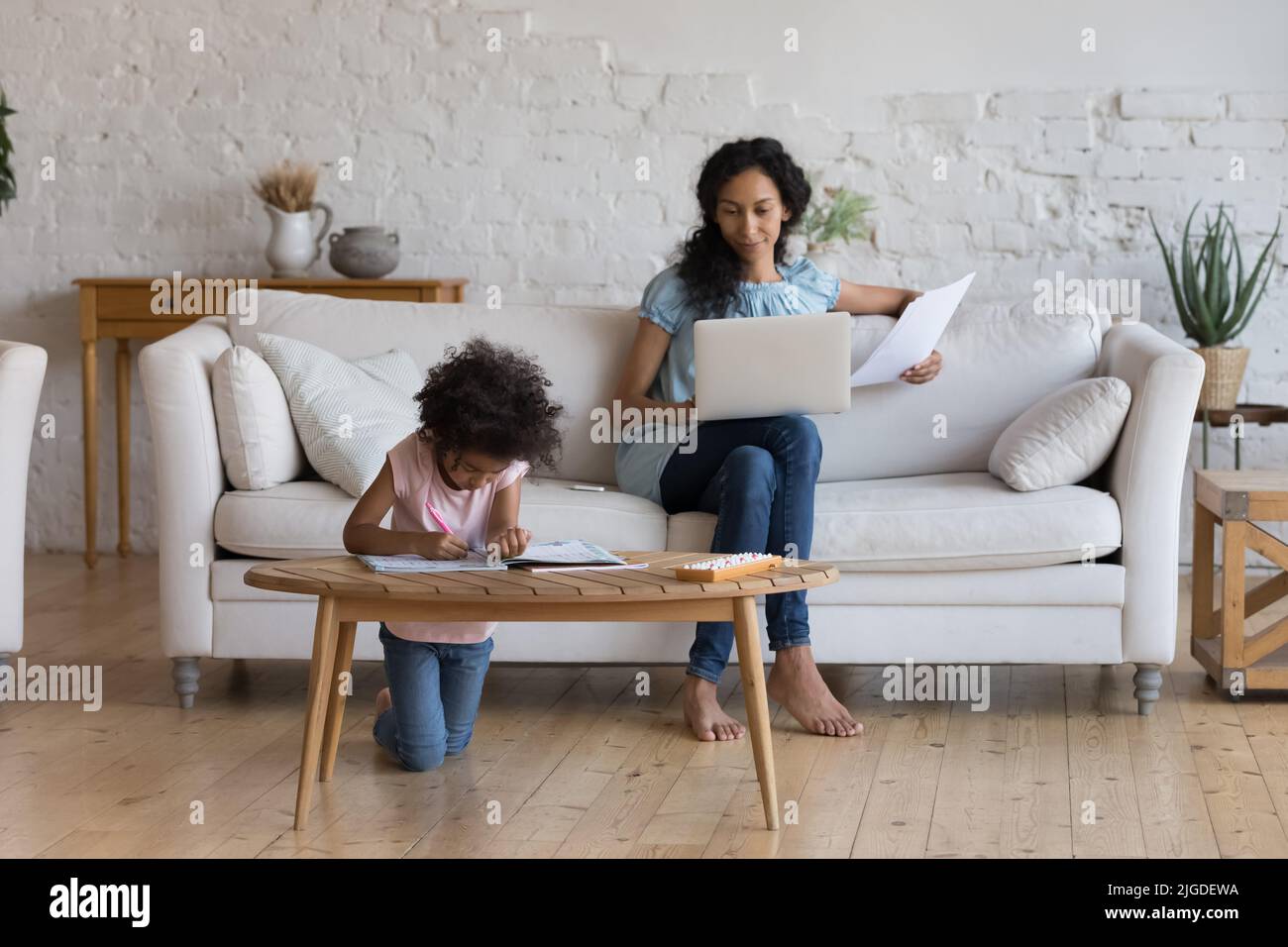 Une mère africaine travaille sur un ordinateur portable, sa fille dessinant assise à proximité Banque D'Images