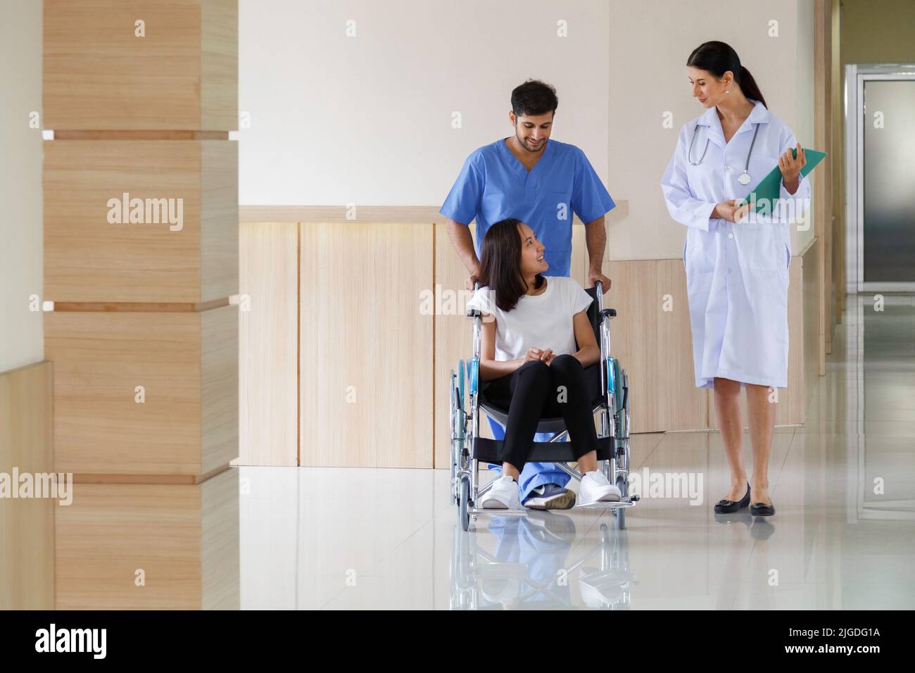 heureuse patiente asiatique souriante assise en fauteuil roulant avec une infirmière masculine parlant au médecin après avoir récupéré un plan de traitement chirurgical à l'hôpital Banque D'Images heureuse patiente asiatique souriante assise en fauteuil roulant avec une infirmière masculine parlant au médecin après avoir récupéré un plan de traitement chirurgical à l'hôpital Banque D'Images
